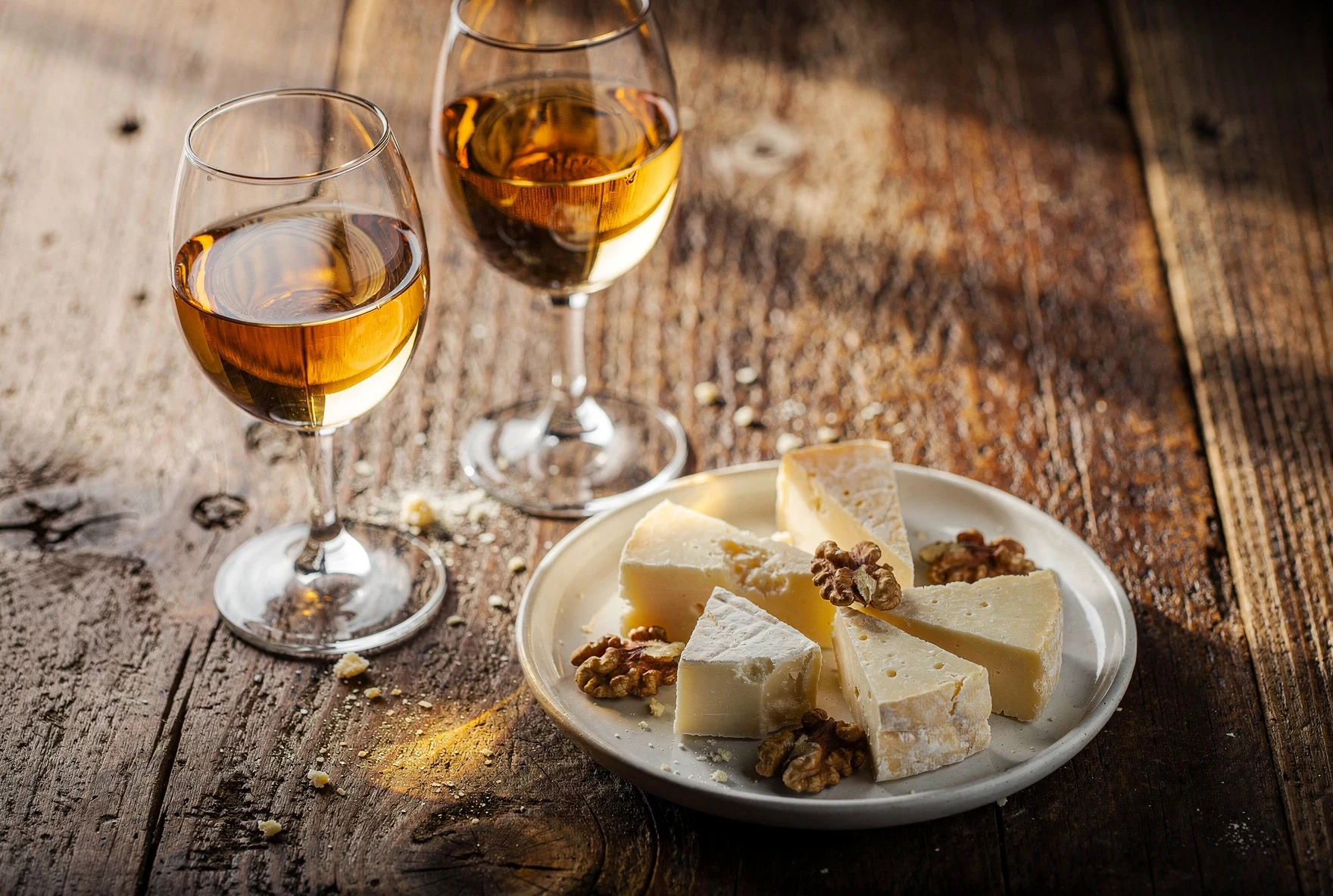 Two glasses of golden amber wine on a wooden table with Georgian cheese and walnuts
