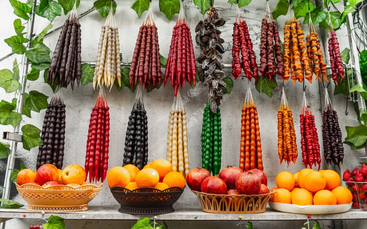 Homemade Georgian churchkhela hanging on strings with walnuts and grapes nearby