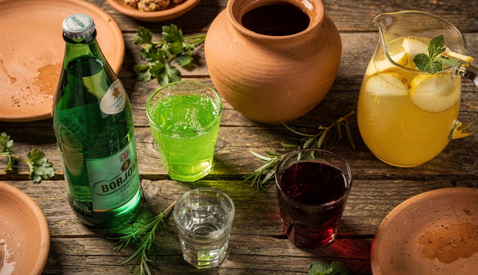 Overhead shot of a Georgian table with an assortment of traditional drinks including Borjomi, tarkhuna, amber wine, chacha, kompot, and lemonade