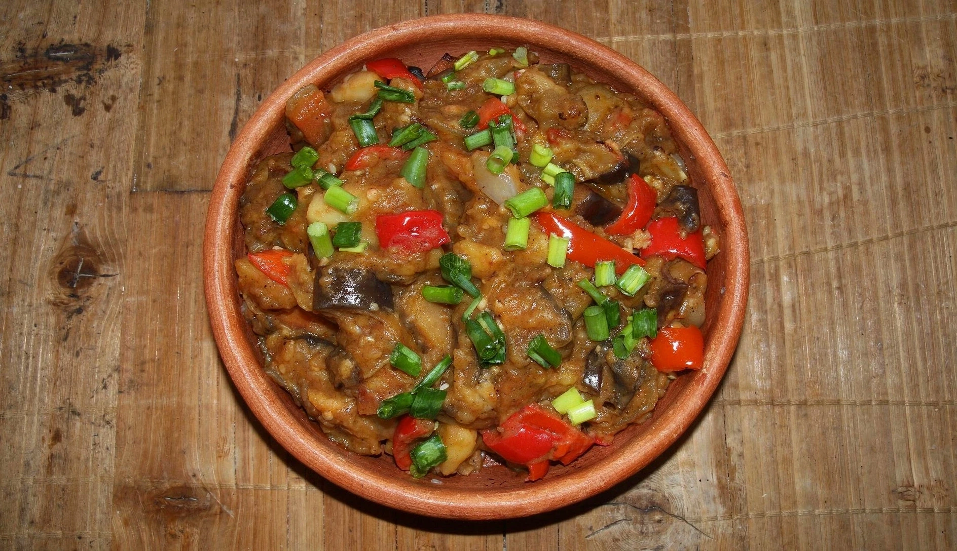 Overhead photo of ajapsandali, Georgian eggplant vegetable stew in a rustic ceramic bowl with fresh herbs