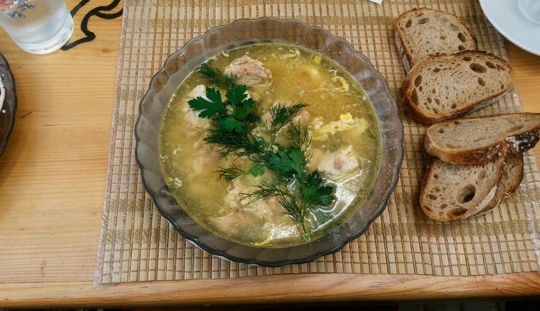 Overhead photo of Georgian chikhirtma chicken soup in a deep bowl with golden broth, shredded chicken, and fresh herbs