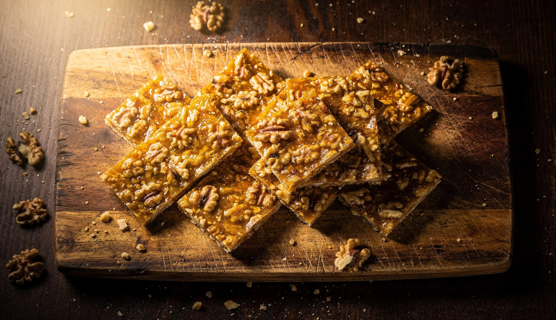 Overhead shot of Georgian gozinaki — golden honey walnut brittle pieces on a rustic wooden cutting board