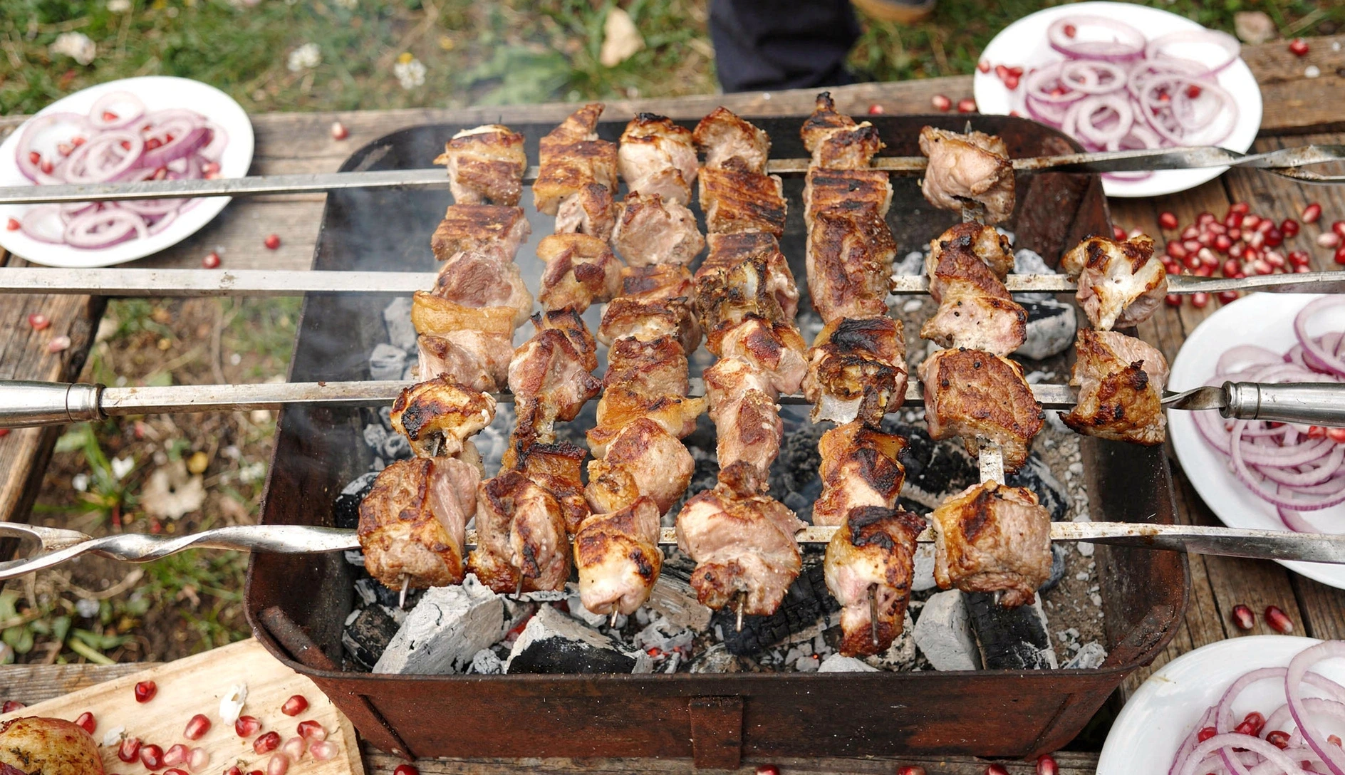 Georgian mtsvadi pork skewers grilling over charcoal embers with onion rings and pomegranate seeds