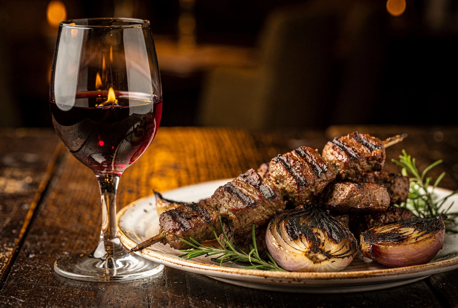 Glass of deep red Saperavi wine next to a plate of grilled mtsvadi with charred onions