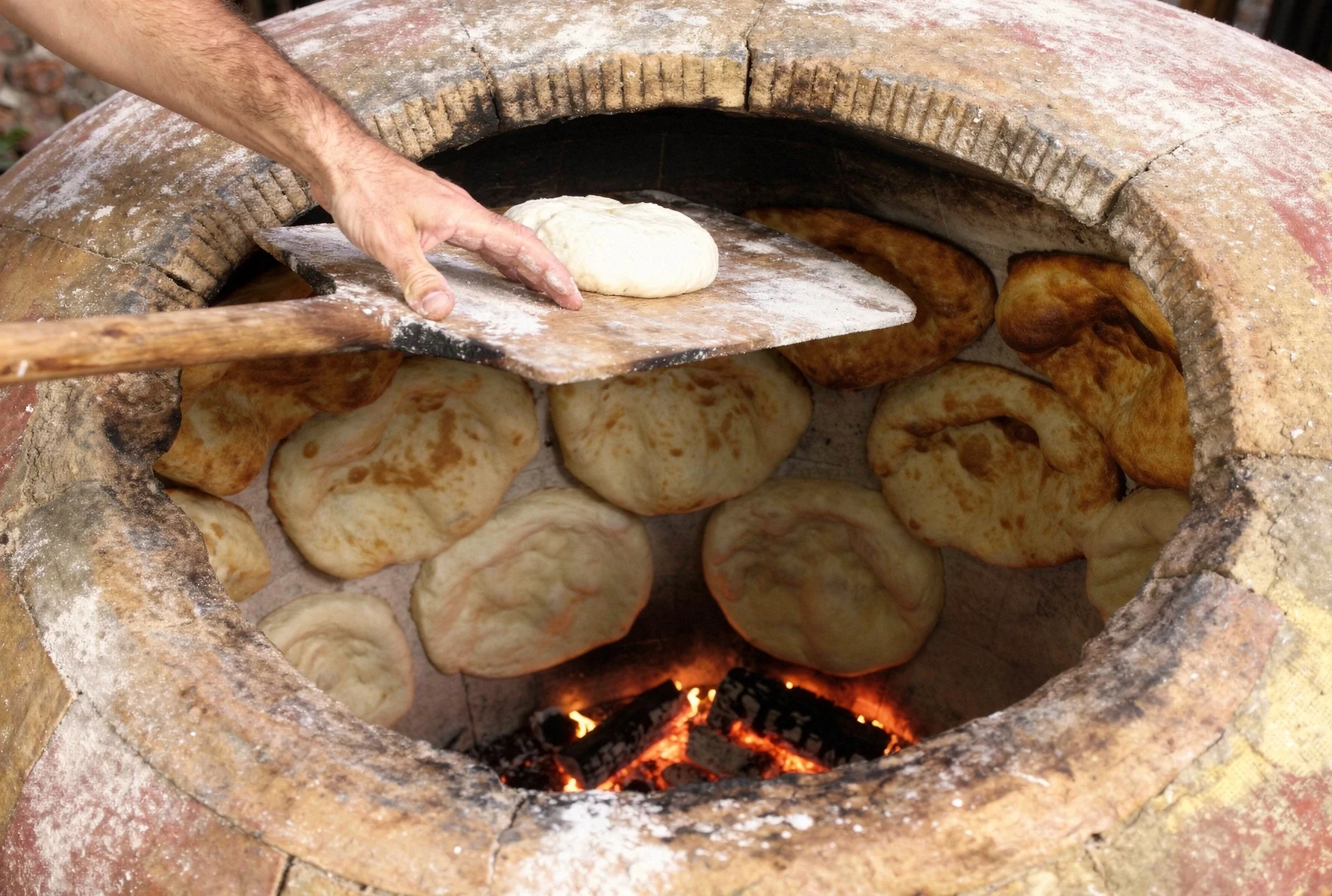 Baker reaching into a traditional Georgian tone oven to bake bread